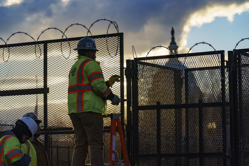 Workers install razor wire atop fencing around the U.S. Capitol perimeter at sunset, in Washington, Monday, Jan. 18, 2021. 
