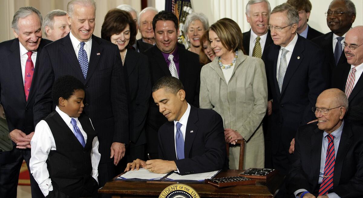 President Obama signing the Affordable Care Act in 2010, surrounded by lawmakers and healthcare activists.
