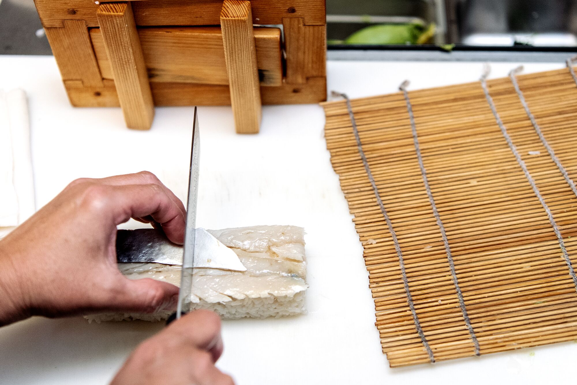 Hands hold a knife cutting a block of sushi.