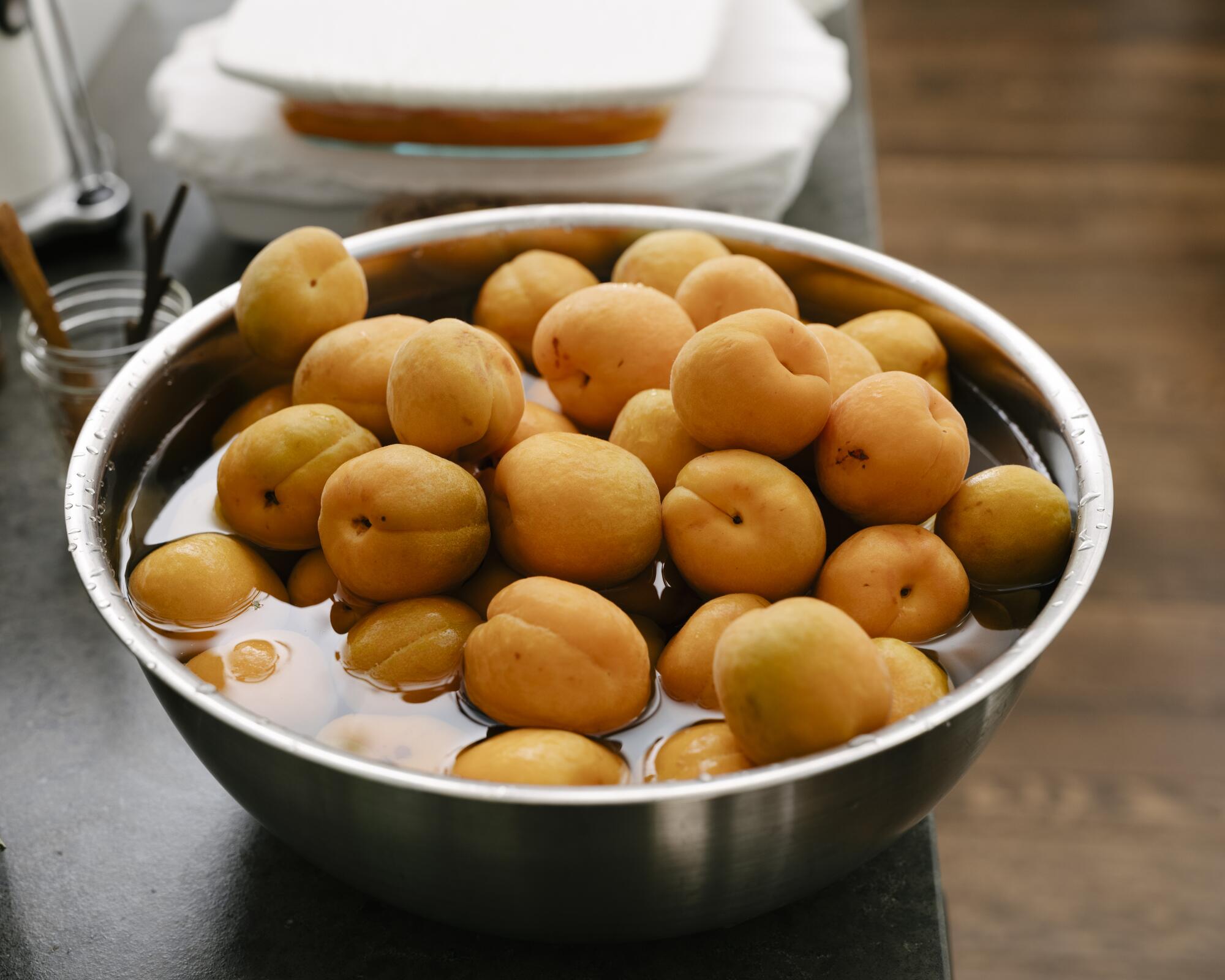A metal bowl holds whole apricots and water.