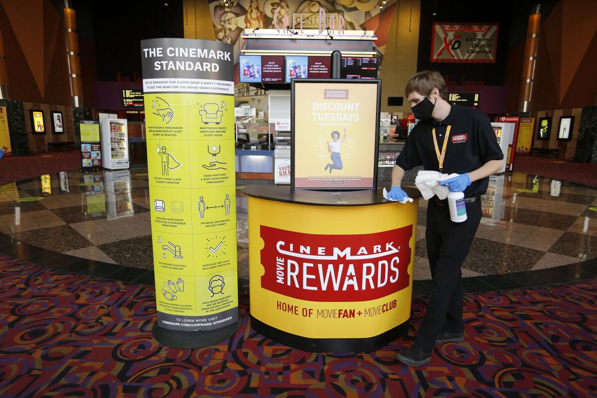 Cinemark Century Cinema employees work to keep the just-reopened theater sanitized, in Huntington Beach on Friday.