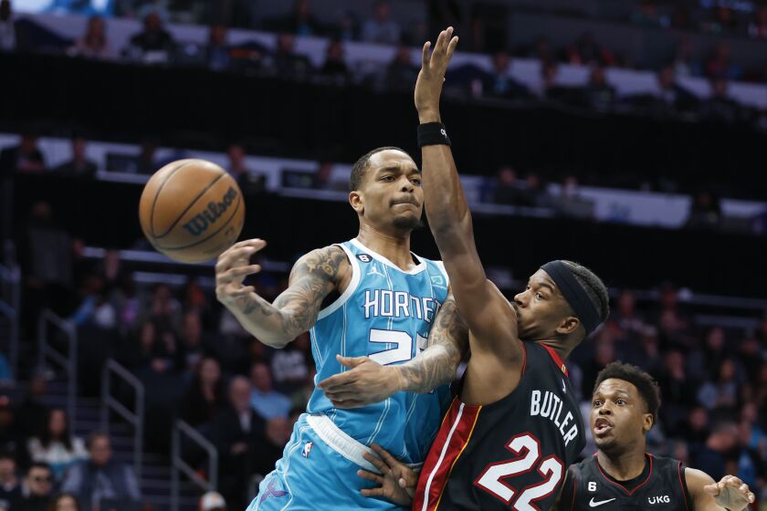 Charlotte Hornets forward P.J. Washington, left, passes around Miami Heat forward Jimmy Butler (22) during the first half of an NBA basketball game in Charlotte, N.C., Sunday, Jan. 29, 2023. (AP Photo/Nell Redmond)