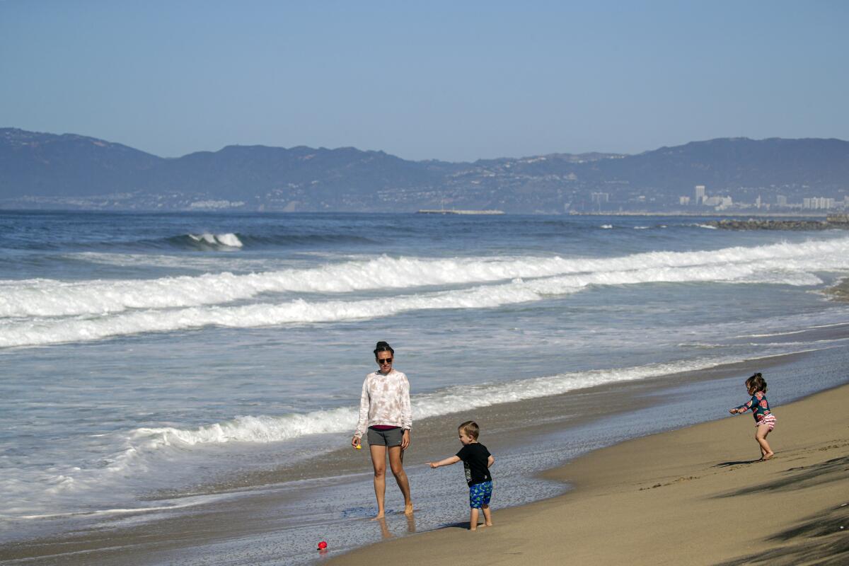 A woman and two children stand at the water's edge on a beach