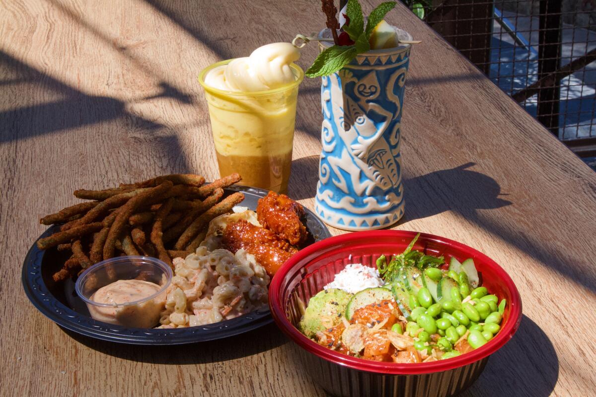 A boozy Dole whip float and tiki drink in the background on a table, a pu pu platter and salmon poke bowl in foreground