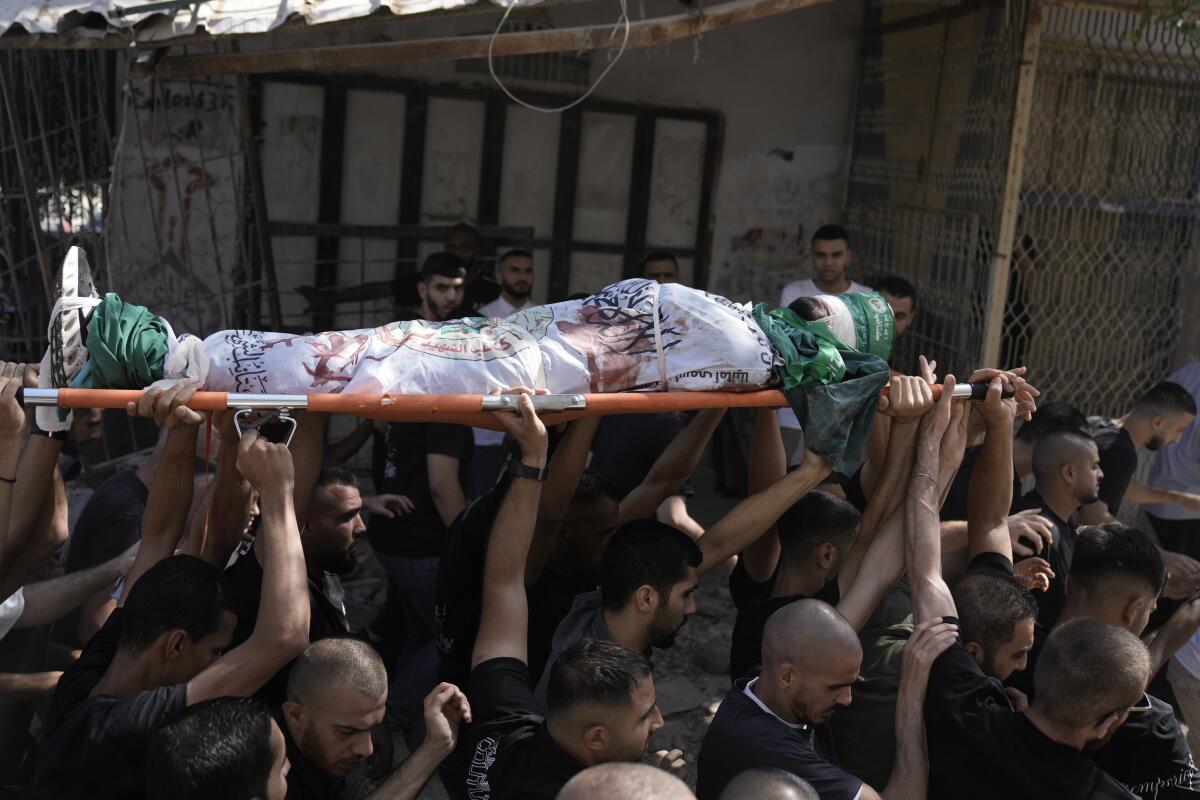 Mourners carry overhead a gurney holding a body wrapped in the Qassam Brigade flag of Hamas' military wing.