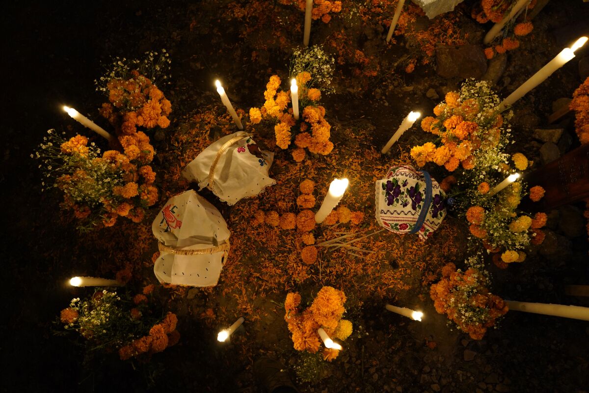 Flowers, food offerings and candles adorn a tomb as relatives spend the night next to the tomb of their loved one during Day of the Dead festivities at the the Arocutin cemetery in Michoacan state, Mexico, Monday, Nov. 1, 2021. In a tradition that coincides with All Saints Day and All Souls Day, families decorate the graves of departed relatives with flowers and candles, and spend the night in the cemetery, eating and drinking as they keep company with their deceased loved ones. (AP Photo/Eduardo Verdugo)