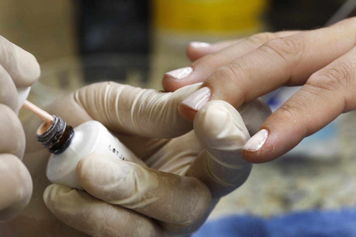 Manicurist David Ngo, wearing gloves, works on the nails of a client on the first day of reopening.