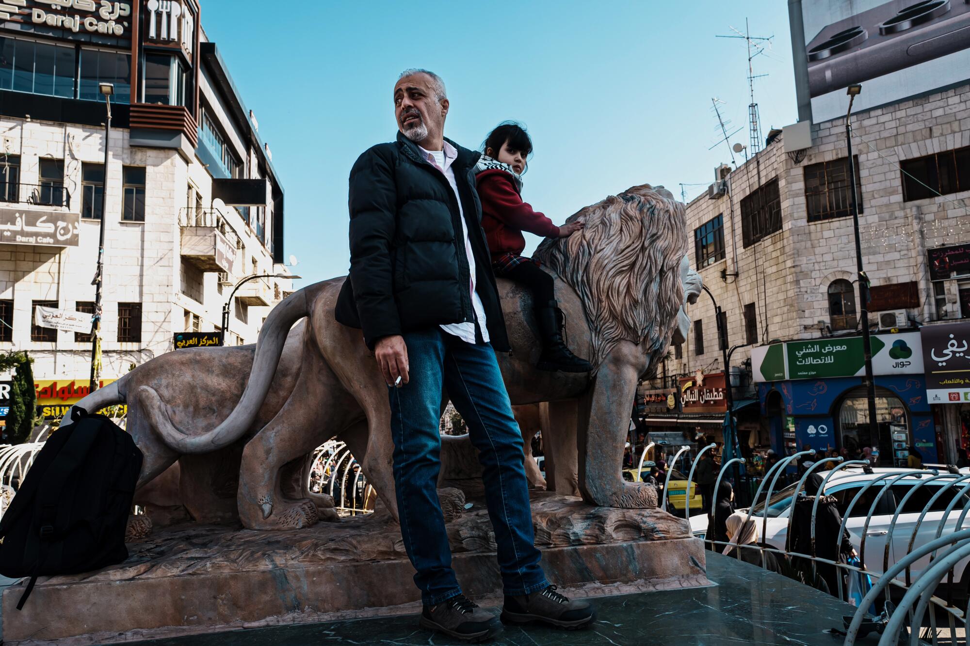 Mohammad Al Farra stands beside his daughter, who is sitting on a lion statue. 