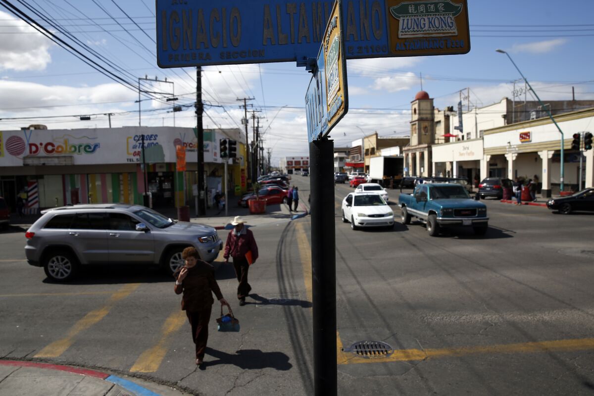 People cross the street under a street sign with both Spanish and Chinese characters in Mexicali, Mexico
