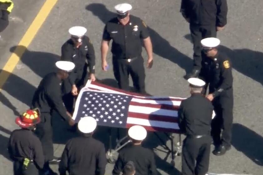 Firefighters place a flag over a recruit, who was killed April 15 on the Hollywood (101) Freeway in Studio City.