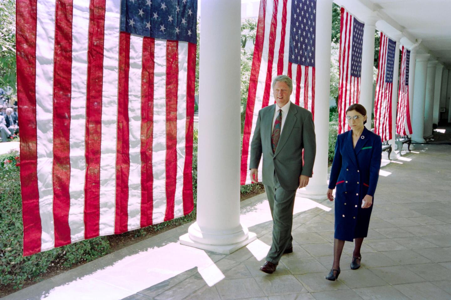 President Clinton and Ruth Bader Ginsburg walk along the outside of the White House in front of hanging U.S. flags