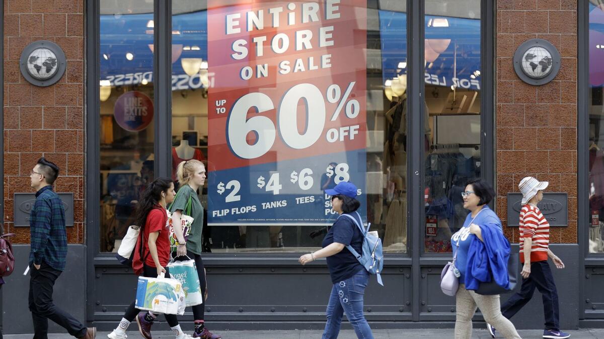 Shoppers in San Francisco walk past a store advertising discounts on July 3.
