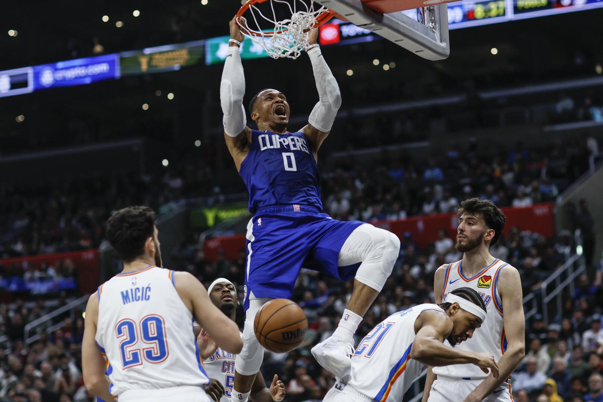 Clippers guard Russell Westbrook hangs on the rim after dunking against the Thunder.