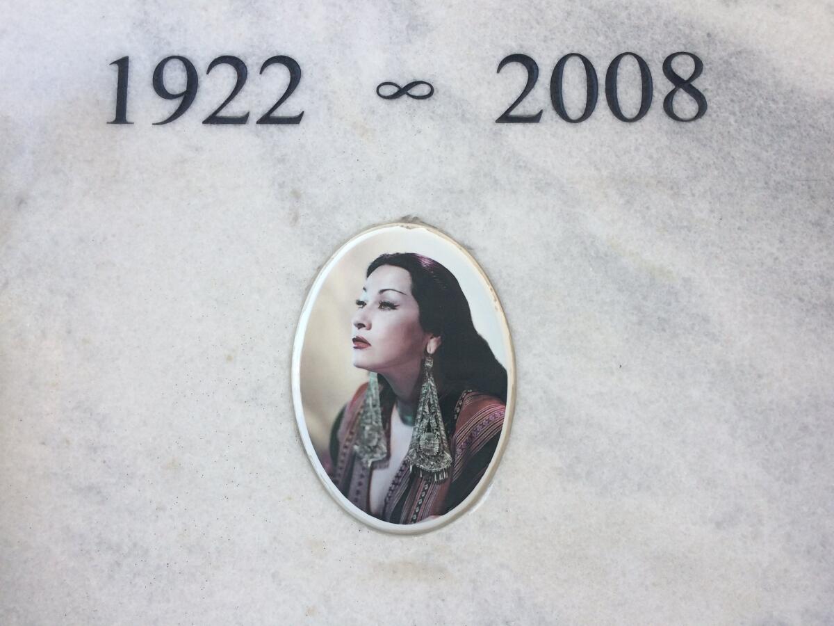 A tomb bears the dates 1922-2008 and features an image of Yma Sumac as a young woman, wearing large, glamorous earrings.