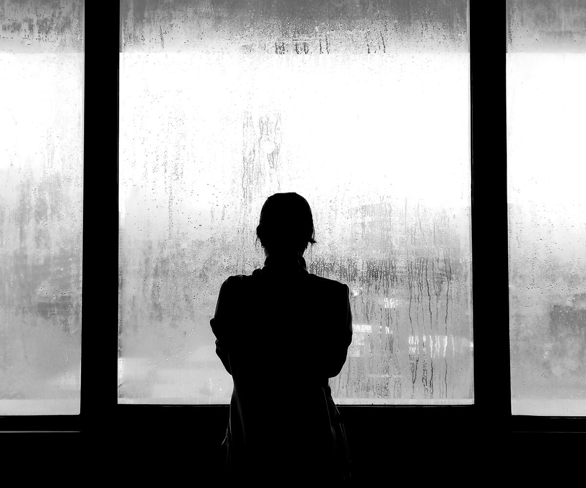 Silhouette of woman outside through a fogged over window. The photo is black-and-white.