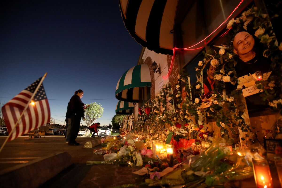 A woman prays at a memorial of candles, flowers and photos outdoors.
