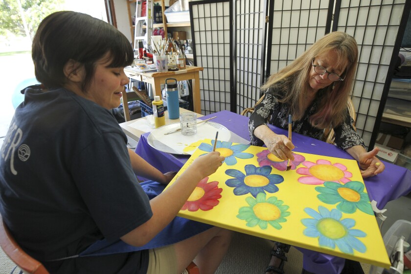 Katie Flores, 24, left, who has autism and local artist Moya Devine work together on a painting titled "Groovy Flowers" which will be part of the Radical Inclusion traveling art exhibition, while in the garage of Devine's Encinitas home on Thursday.