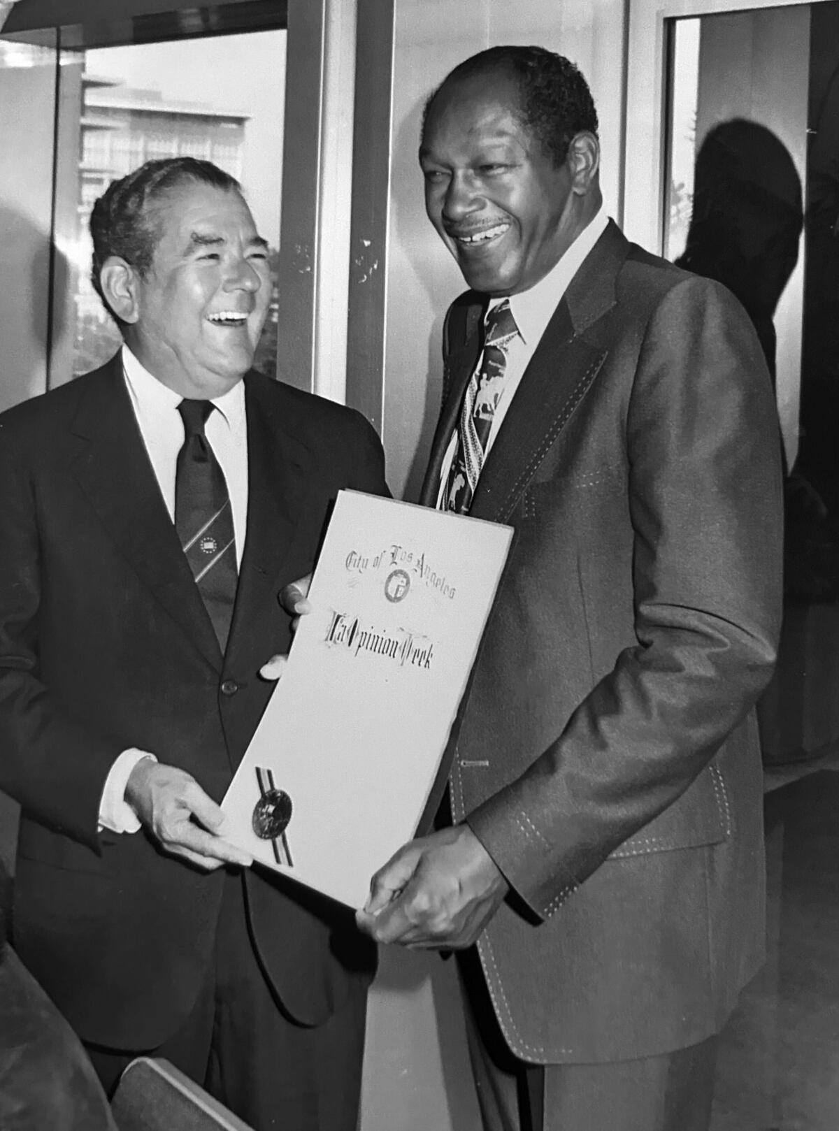 A black-and-white photo of Ignacio Lozano Jr. and former L.A. Mayor Tom Bradley standing and holding an official document