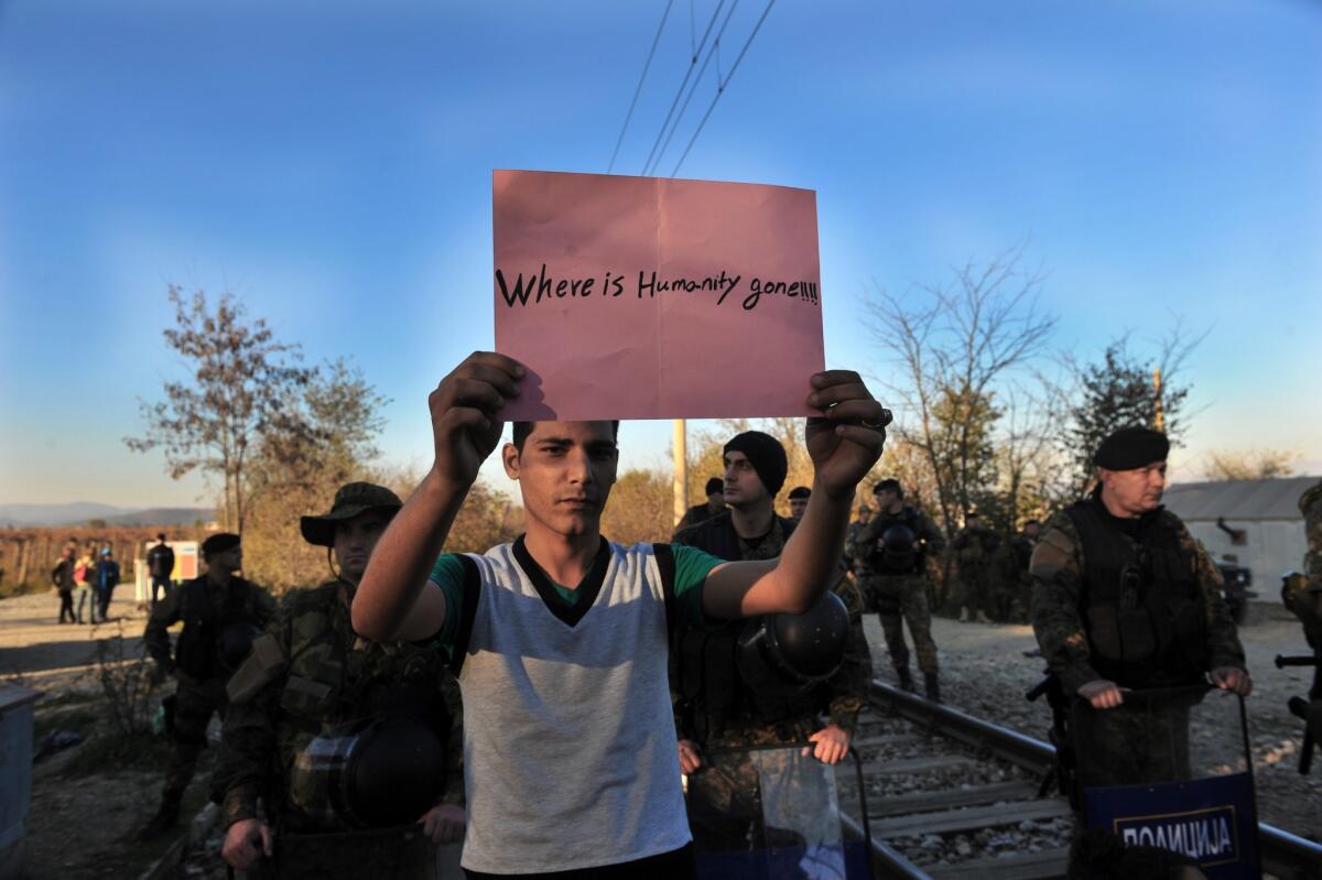 A man holds up a sign as migrants and refugees cross the Greece-Macedonia border on Nov. 19.