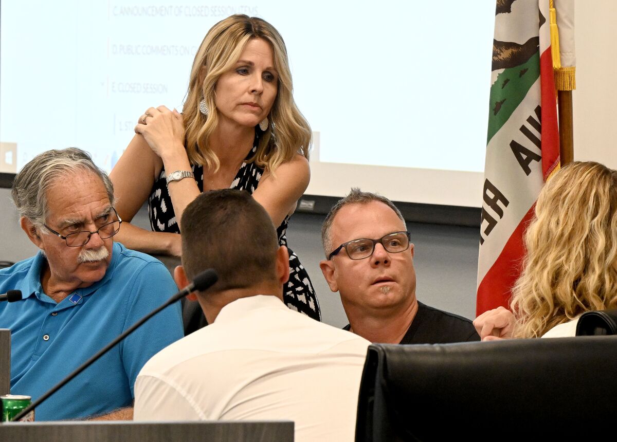 Five people at the front of a meeting room huddle near the California state flag for a discussion