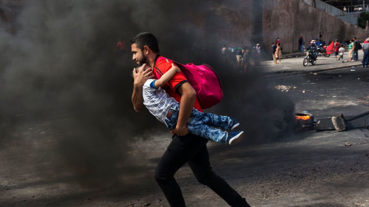 A man carries his son Dec. 1 across a burning barricade erected by supporters of presidential candidate Salvador Nasralla protesting official election results in Tegucigalpa, Honduras.