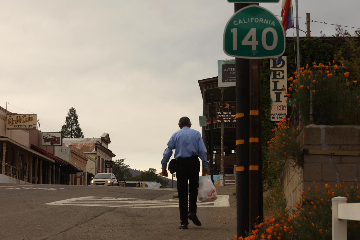 Man walks on road next to deli and California highway signs