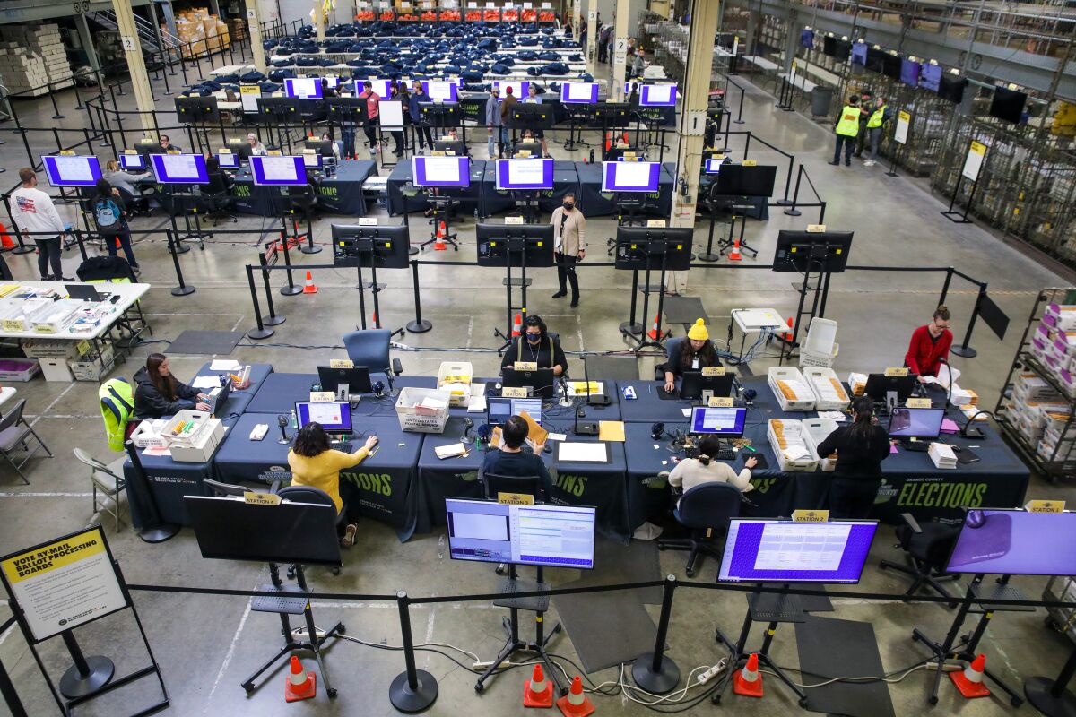 Several people sit at desks sorting ballots in a large facility