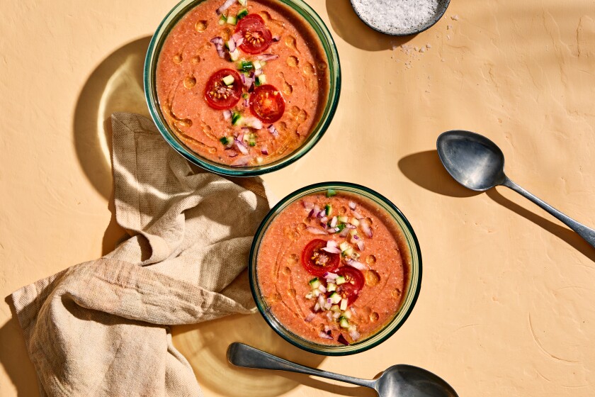 An overhead view of two bowls of reddish soup sprinkled with diced vegetables and slices of tomato.