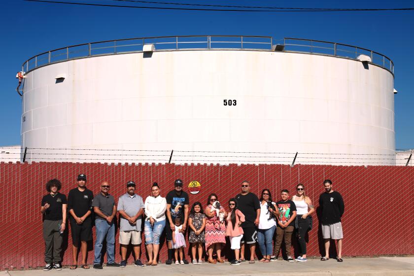 CARSON, CA - NOVEMBER 12, 2021 - - Four generations of the Saldana family stand across the street from their home on 1238 E. 213th in Carson against a backdrop of the Shell oil tank farm on November 12, 2021. The Saldana family, 30-strong, ome not photographed here, have lived across from the Shell oil tank farm and near the Dominguez Channel for decades. They have all been relocated to hotel rooms due to the odor from the nearby Dominguez Channel that was making their family and many residents in the area sick. They talk about years of worries and new anger over the latest environmental assault on their family and community. (Genaro Molina / Los Angeles Times)