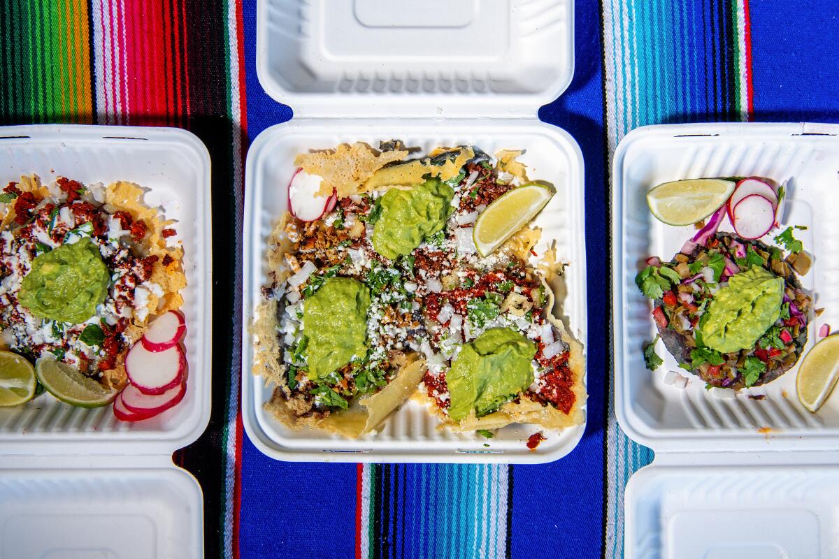 An overhead photo of three to-go boxes of loaded tacos on colorful cloth background