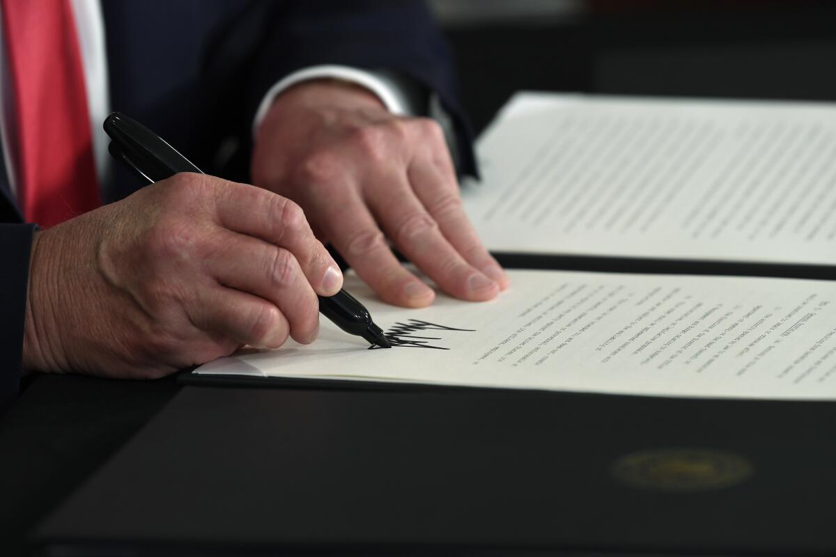 A close-up image of Trump's hands shows him signing an executive order 