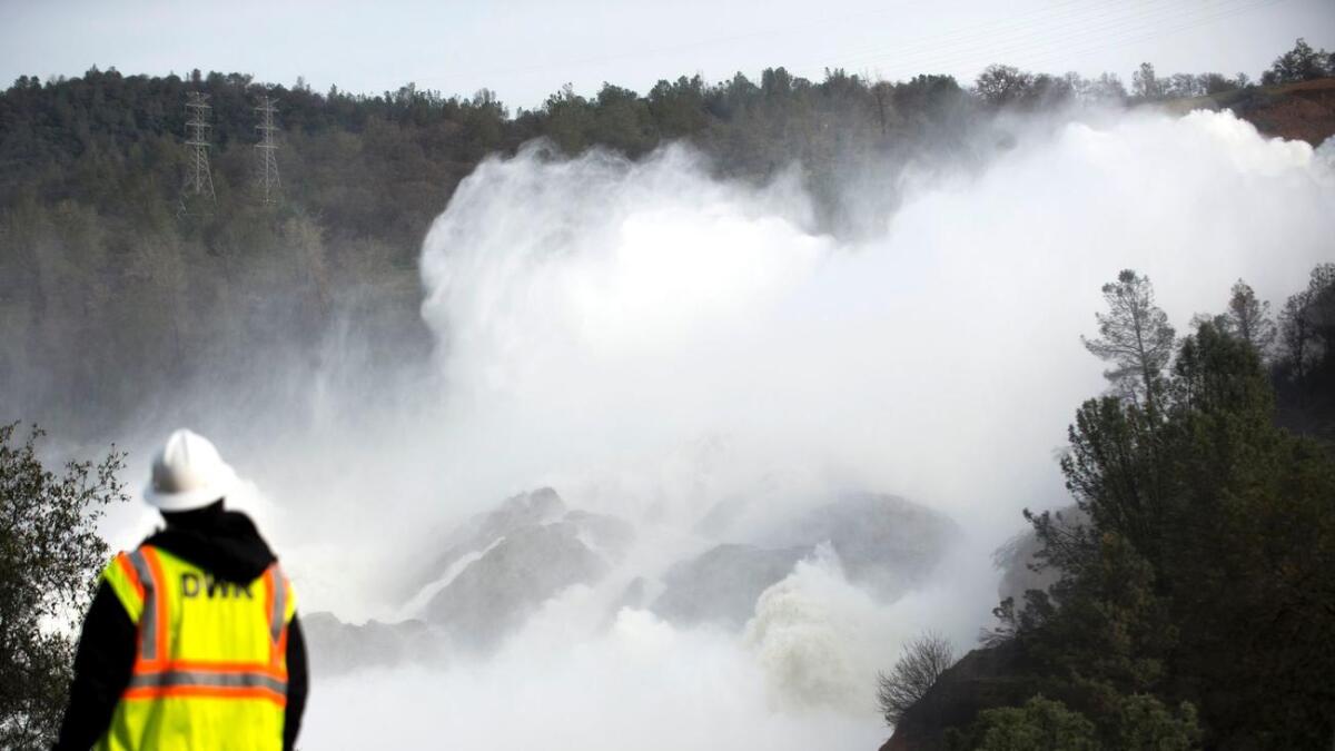 A utility worker looks toward water being released down an amergency spillway at the Oroville Dam.