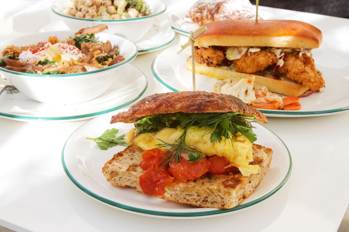 A spread of dishes from all-day cafe Highly Likely on a white tabletop: a tomato-and-herb-topped breakfast sandwich in front