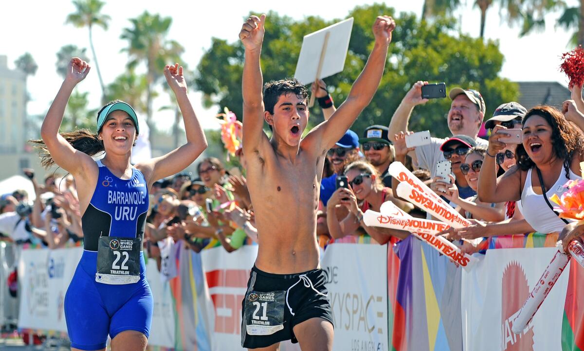 Spectators cheer as the winner of the women's division, Florencia Barranque, from Uruguay, runs next to teamate Damian Barrera as they cross the finish line in the triathlon during the Special Olympics in Long Beach on Sunday.