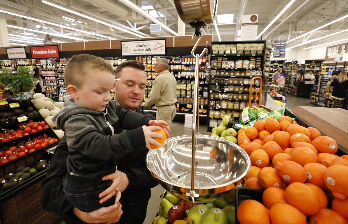 Zachary Reitz, who has vacationed on Catalina Island since he was a child, holds his 3-year-old son Jace Reitz as he weighs fruit at the new Vons Avalon Market. (Al Seib / Los Angeles Times)