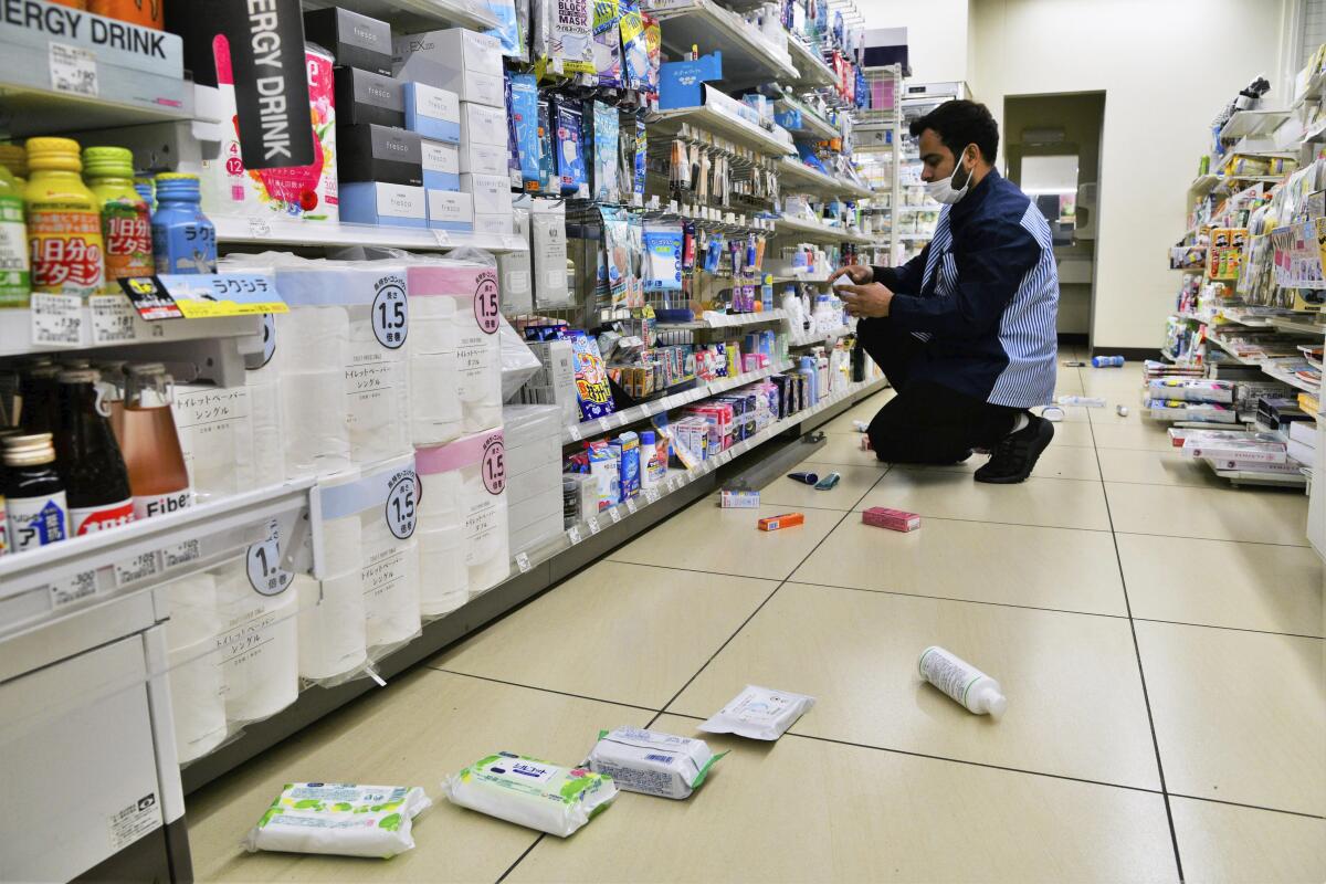 A man kneels in a store aisle picking up a few fallen items.
