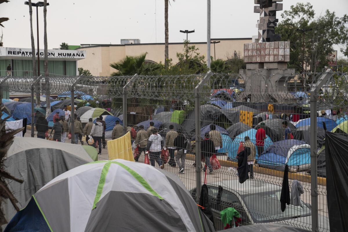 Migrantes regresados a México caminan junto a un campamento donde viven los solicitantes de asilo