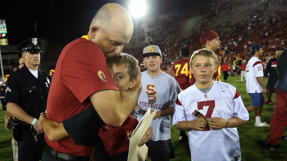 Interim USC coach Clay Helton kisses his son, Turner, at midfield after the Trojans beat Utah 42-24 at the Coliseum on Oct. 24, 2015.