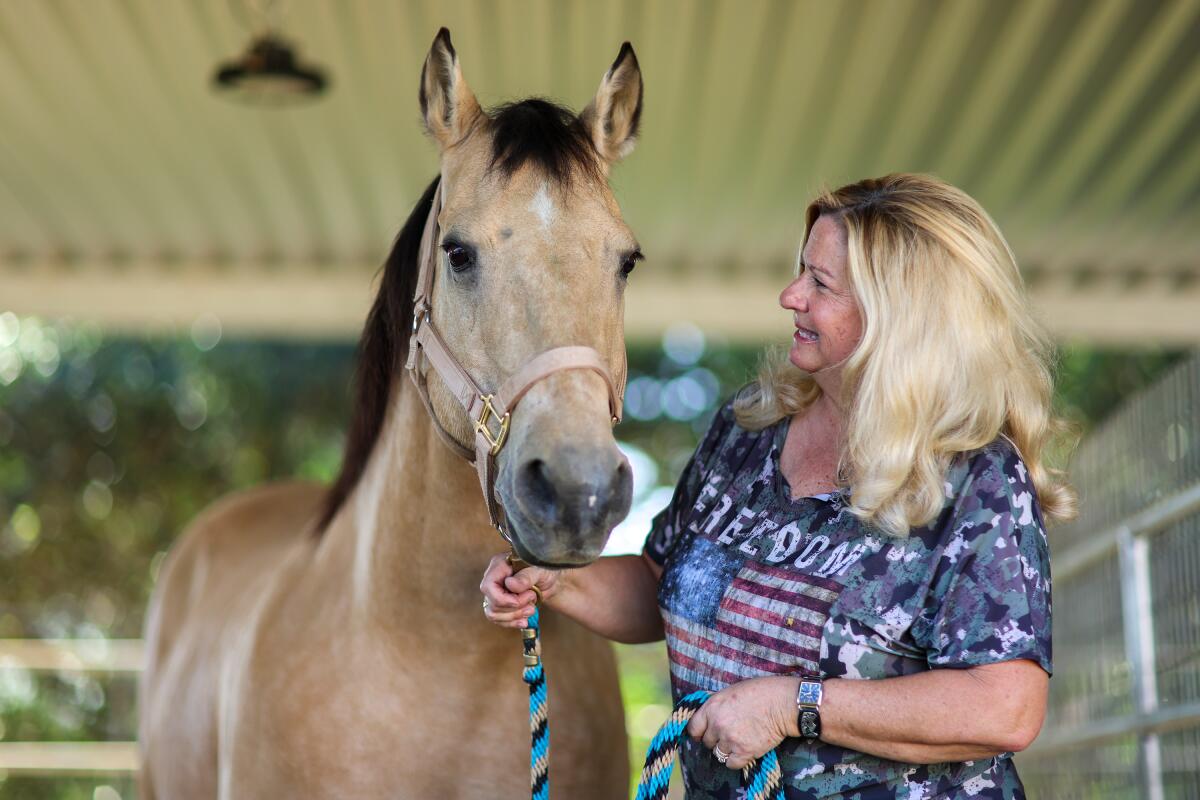 A woman holds a rope under a horse's mouth as it stands next to her.