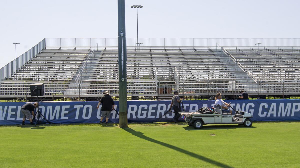 Crew members run wire cables in front of the stands at the field where the Chargers will hold practice at the Jack Hammett Sports Complex in Costa Mesa.