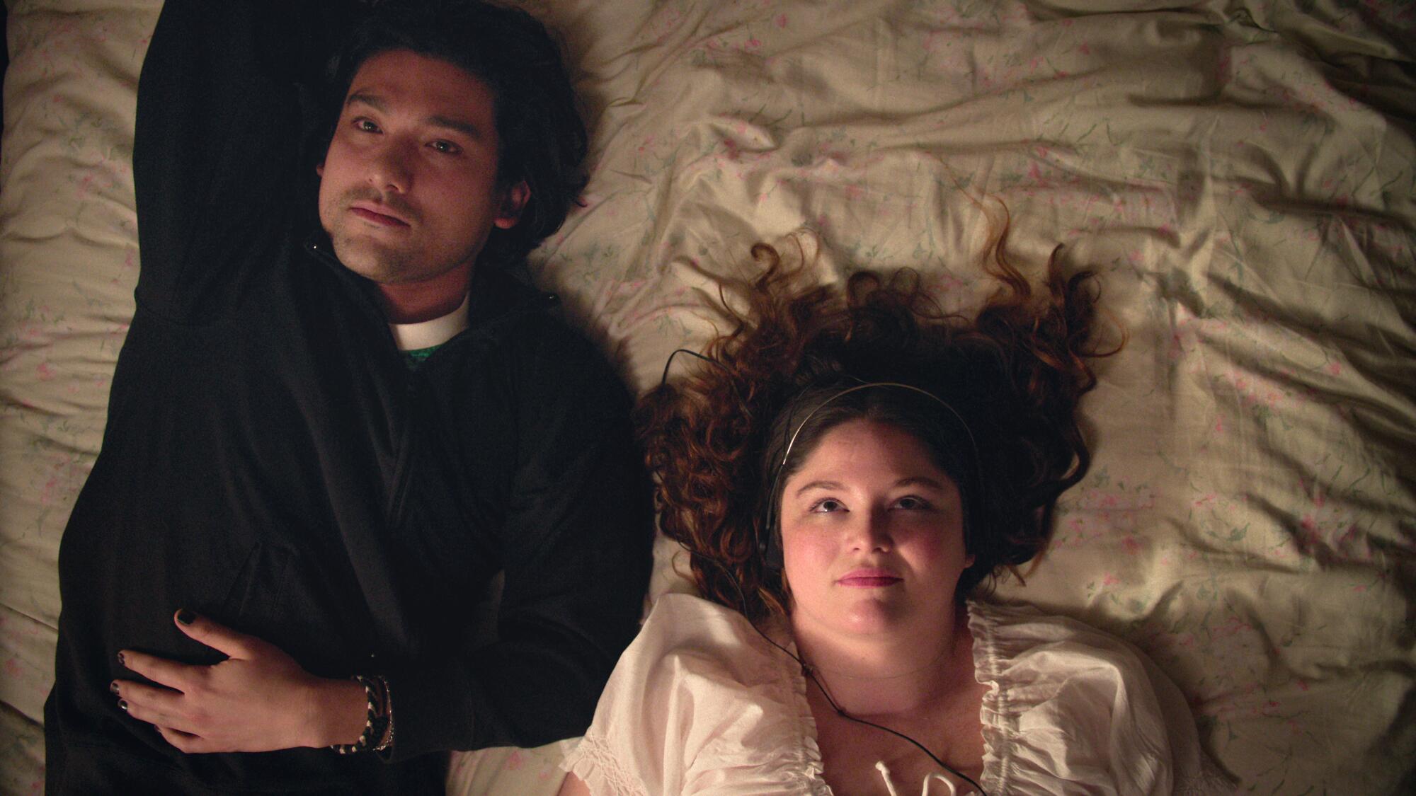 A man in black lays on a bed next to a woman in white
