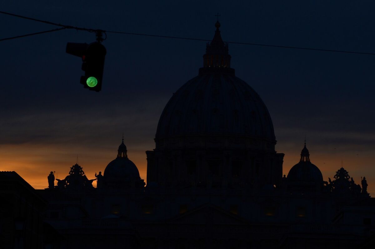 A green traffic light is shown next to the silhouette of St. Peter's basilica at night.