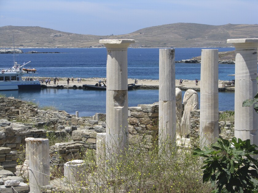 Ancient statues and columns of a house rise just above the landing quay in the archaeological park of Delos, Greece.