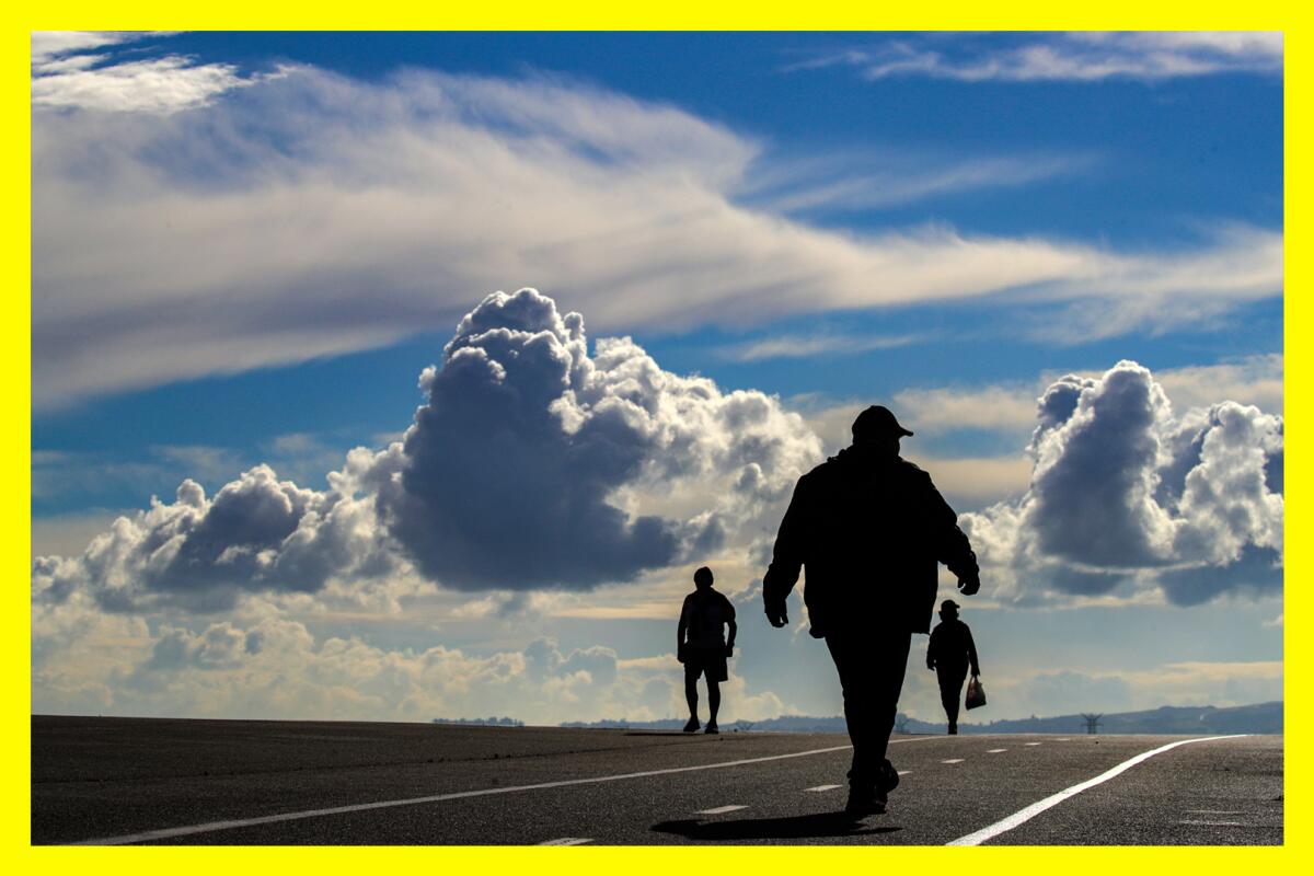 Three people in silhouette walking along a trail with a partly cloudy sky behind them.