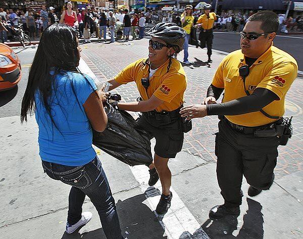 Alondra Alonzo, center, a Business Improvement District security officer, wrests a bag of rabbits from Stacy Martinez, who was trying to sell them on Maple Avenue in downtown Los Angeles. Sgt. Ernesto Mahano, right, arrives to assist.