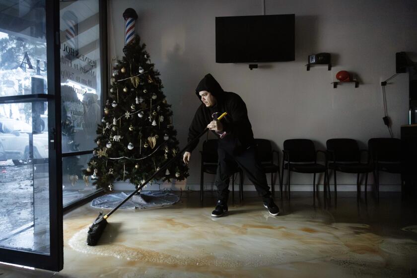 El Mirage barbershop owner Michael Ramirez sweeps away water on Thursday, Dec. 21, 2023 in Port Hueneme, CA.