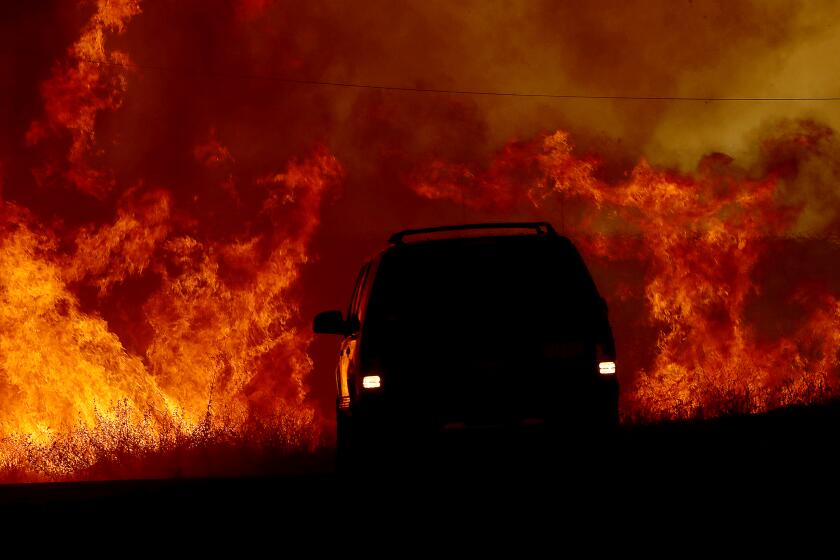 A motorist drives past flames from the Fairview fire along Batista Road near Hemet.