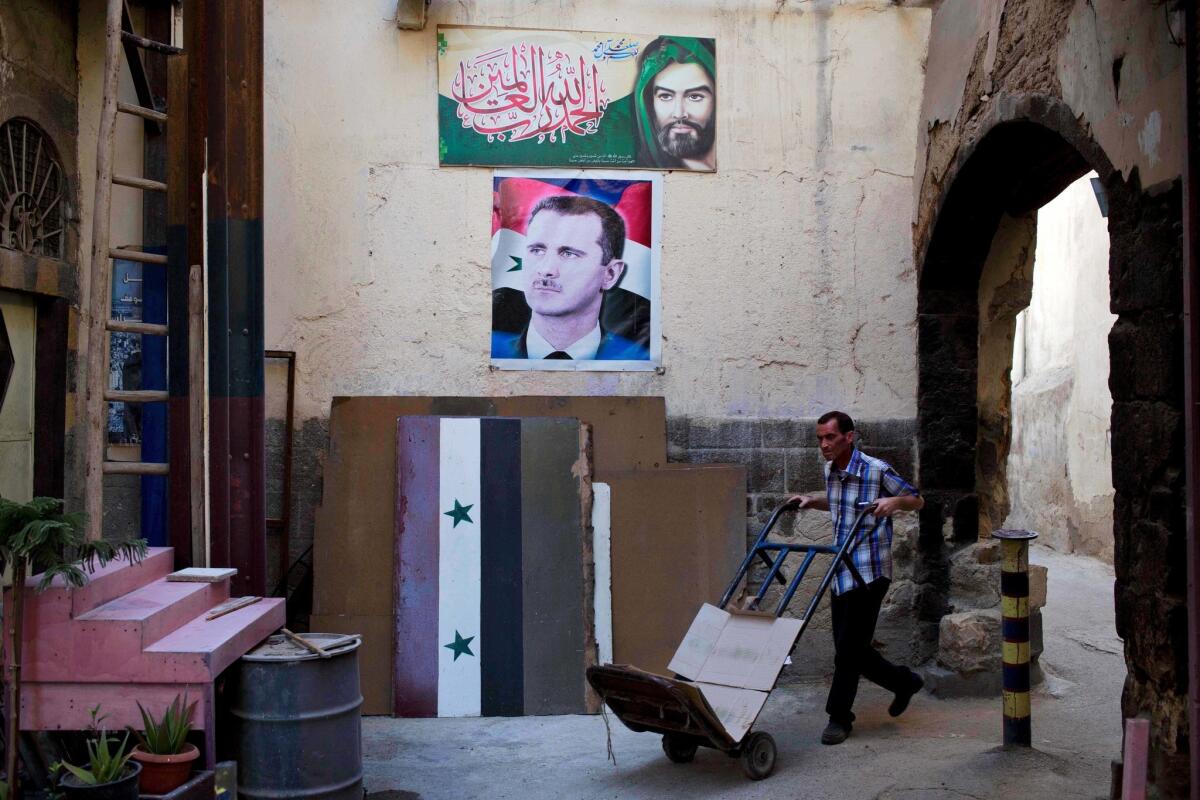 A Syrian goes about his work under a portrait of President Bashar Assad and the national flag in Damascus' Old City on April 17, 2016.