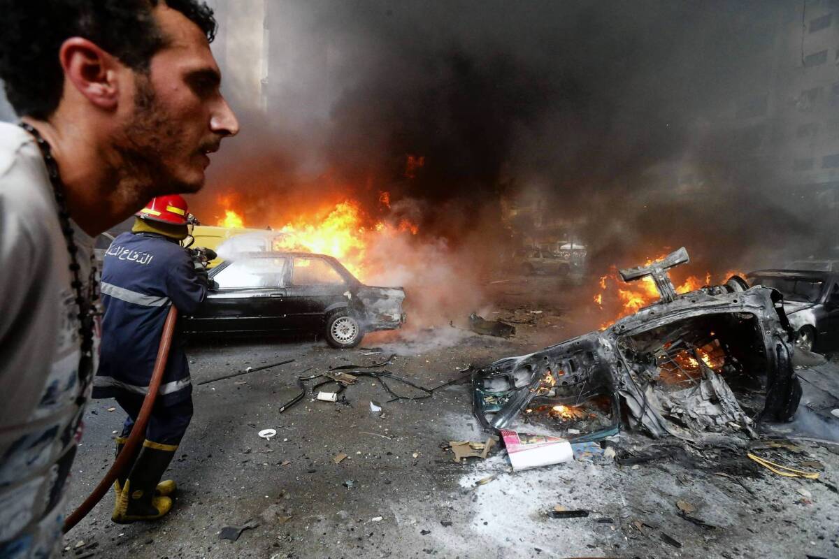 A man walks past as a firefighter works to extinguish the blaze at the site of a car bombing in south Beirut.