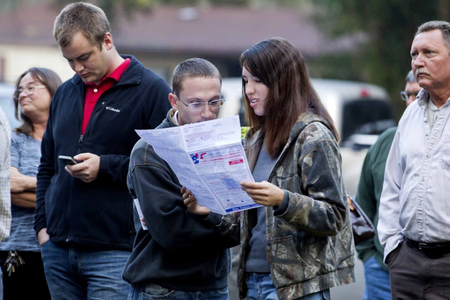Robert Ceska, third from left, and Meagan Lewis look over a sample ballot just after dawn as people line up at the County Polling House in Crawfordville, Fla.